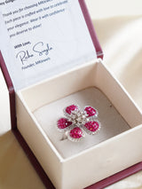 five‑petal ruby baguette flower cocktail ring edged with white crystals on adjustable band
