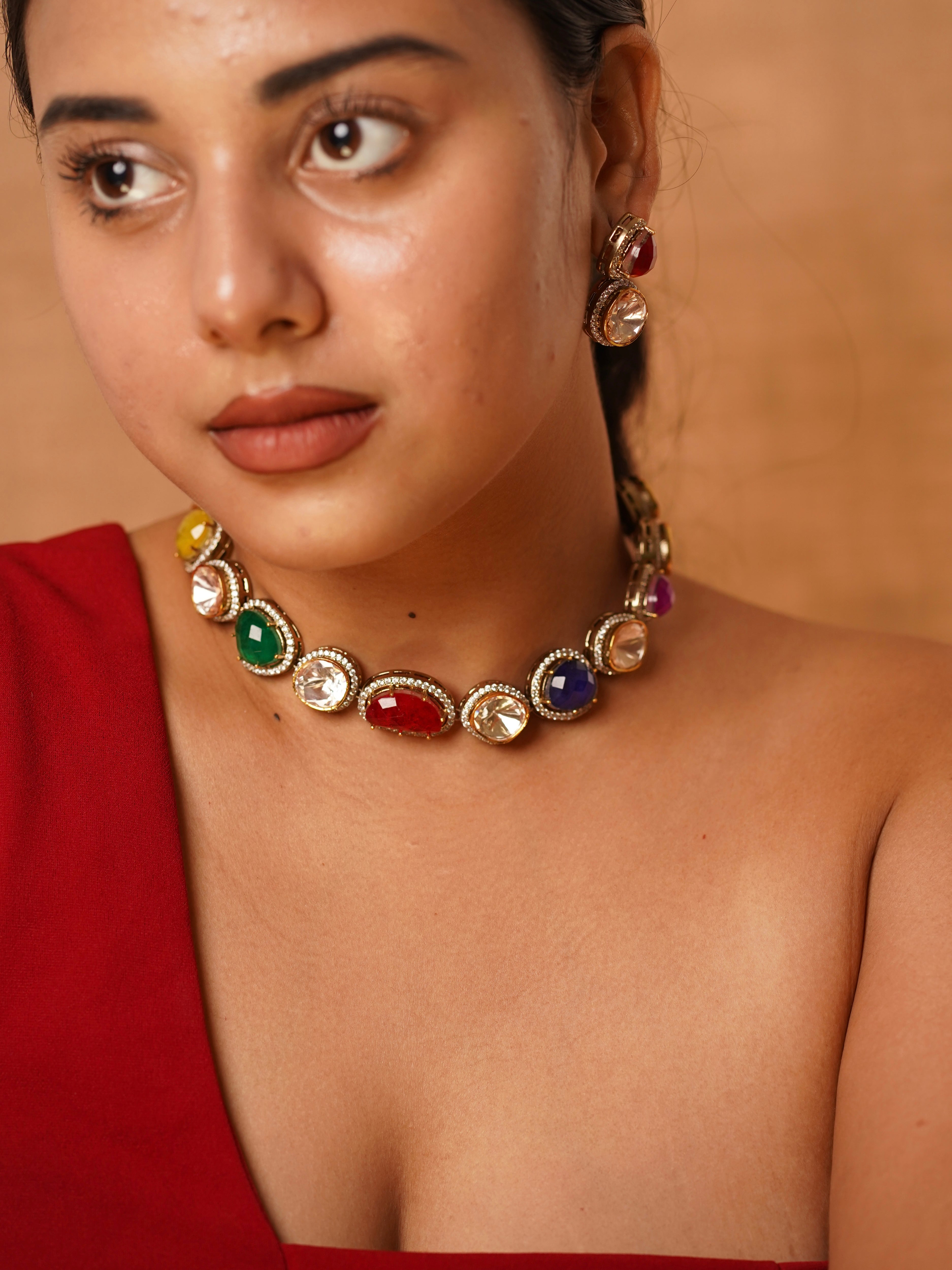 Model wearing navratna statement set with multicoloured gemstones bordered by polki detailing and matching earrings