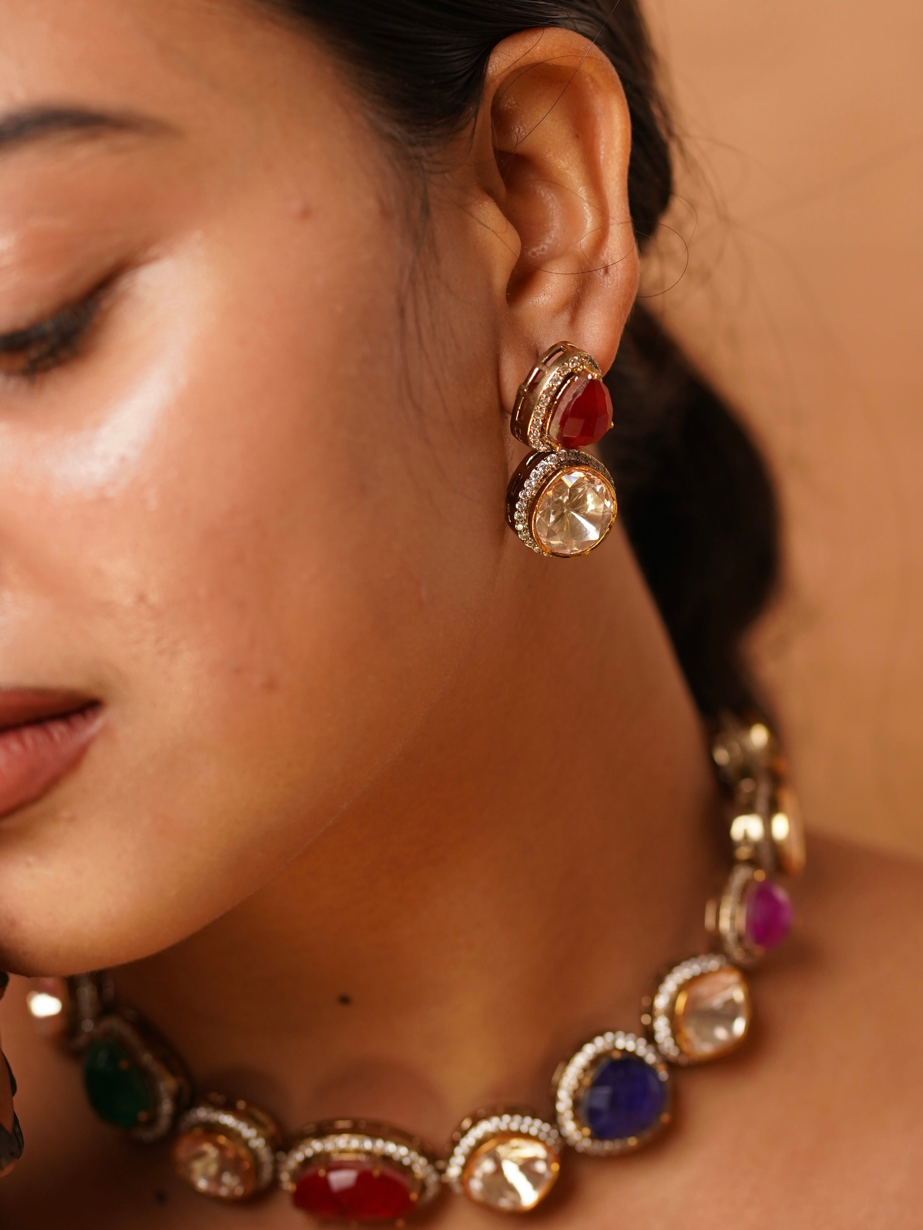 Close-up of navratna statement earring with layered red and clear stones bordered by polki accents