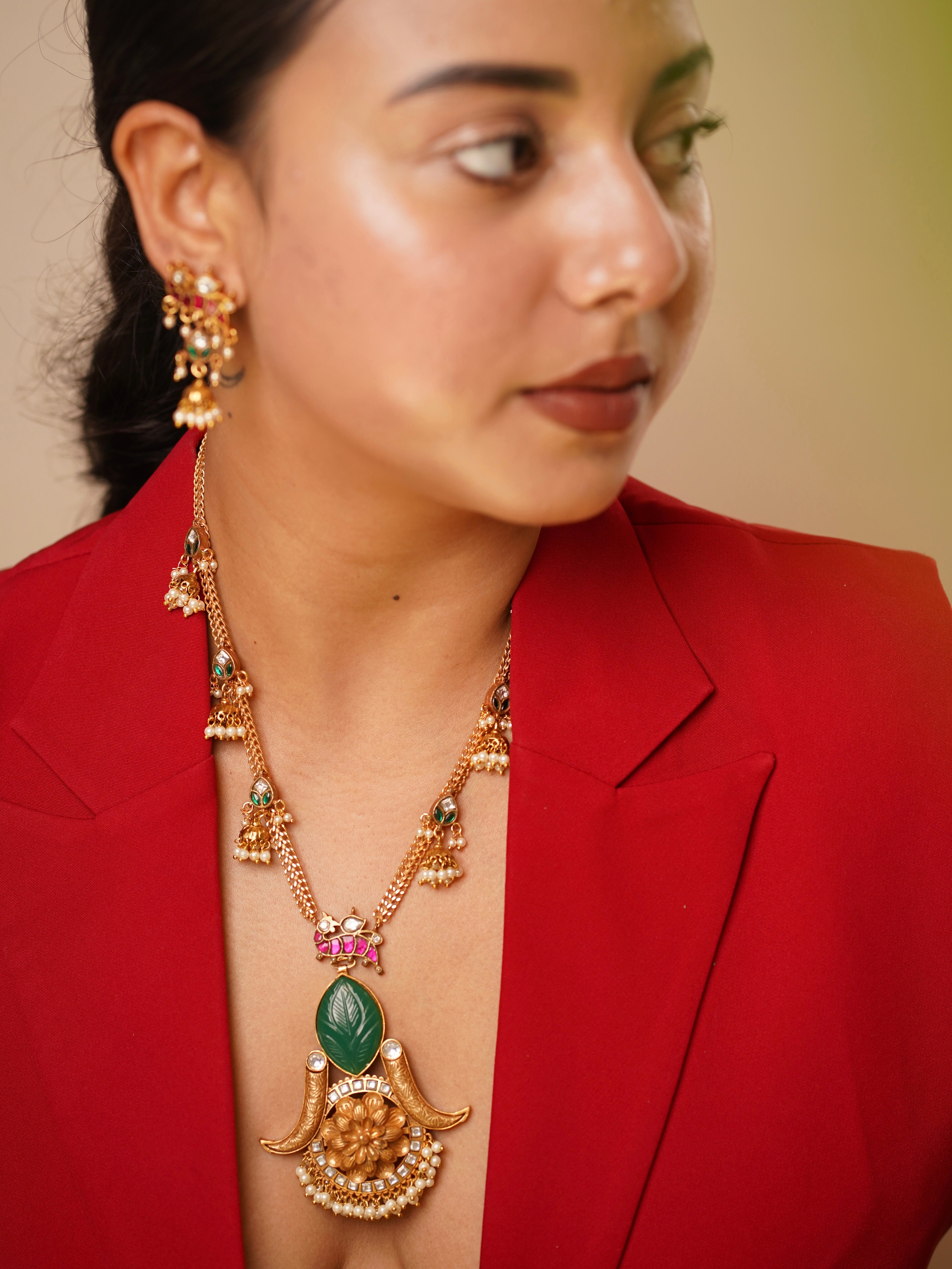 Gold-plated necklace with carved green leaf motifs, ruby accents, and jhumka earrings