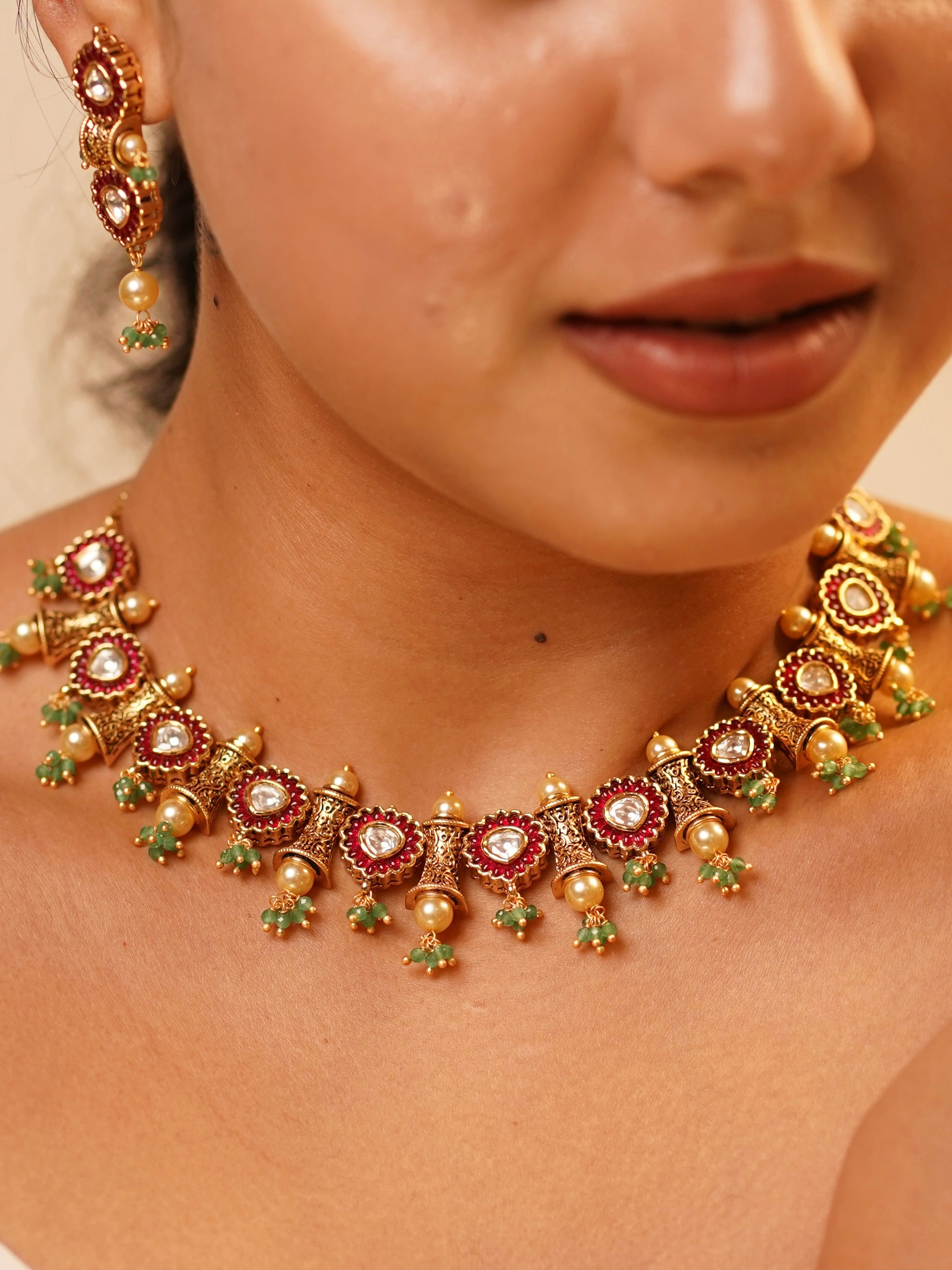 Close-up of kundan necklace featuring golden pearls and red-green enamel details