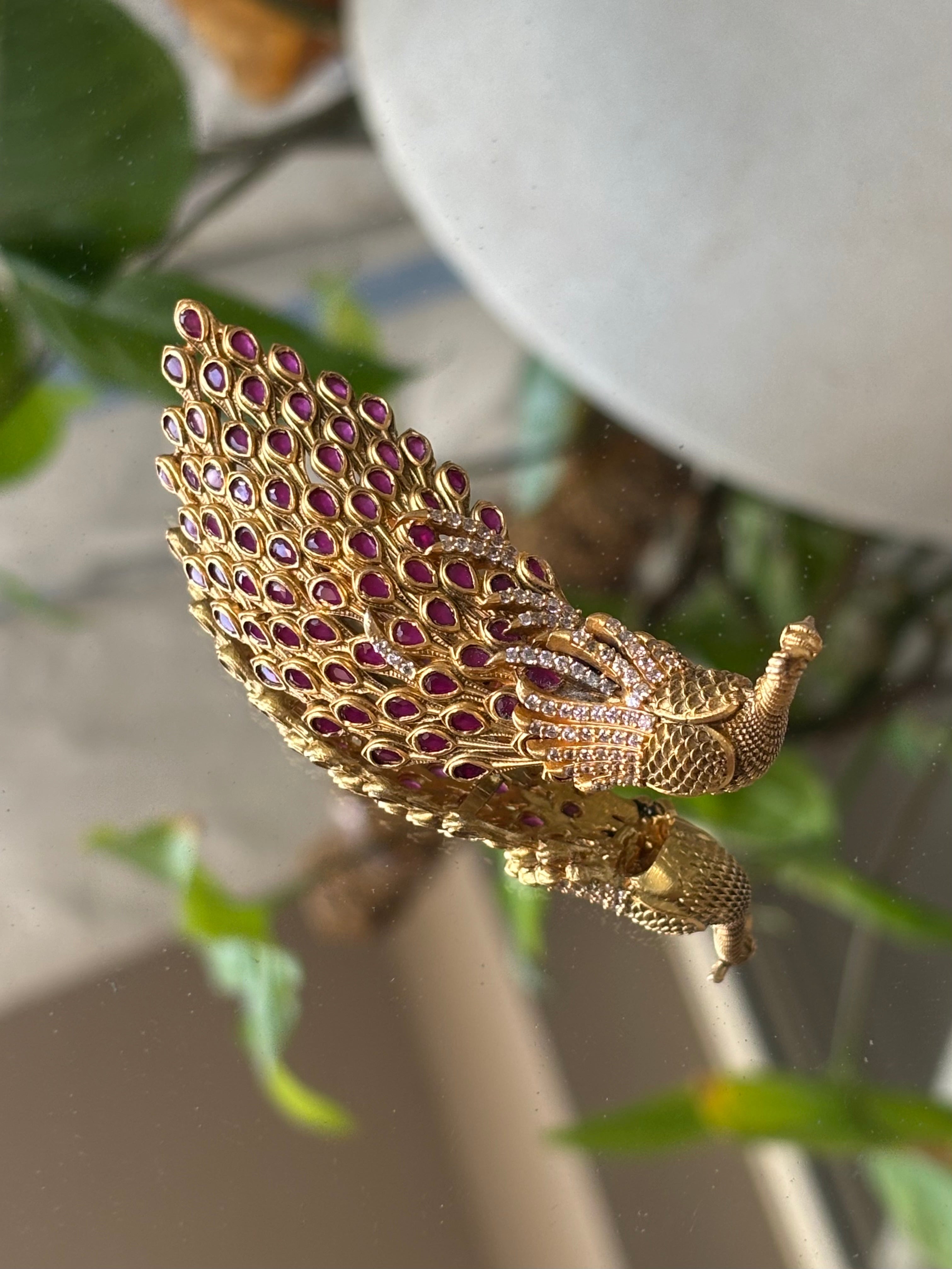 Top view of ornamental peacock brooch with curved shape and vibrant gem-like accents