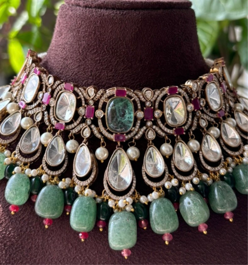 Angled view of kundan necklace set with ruby and green gemstone accents and pearl drops