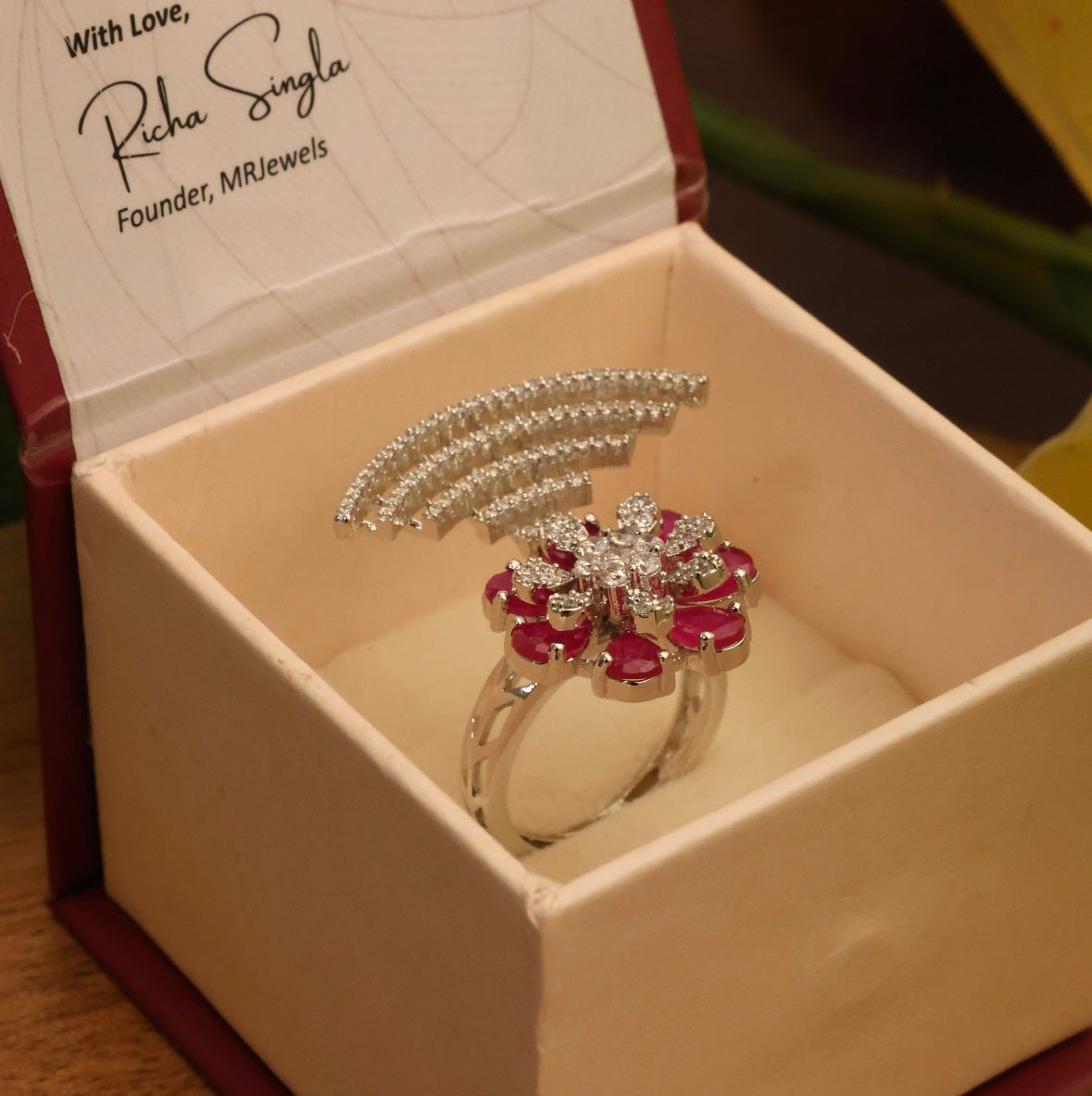 Angled side view of floral statement ring with shimmering diamonds and red stones