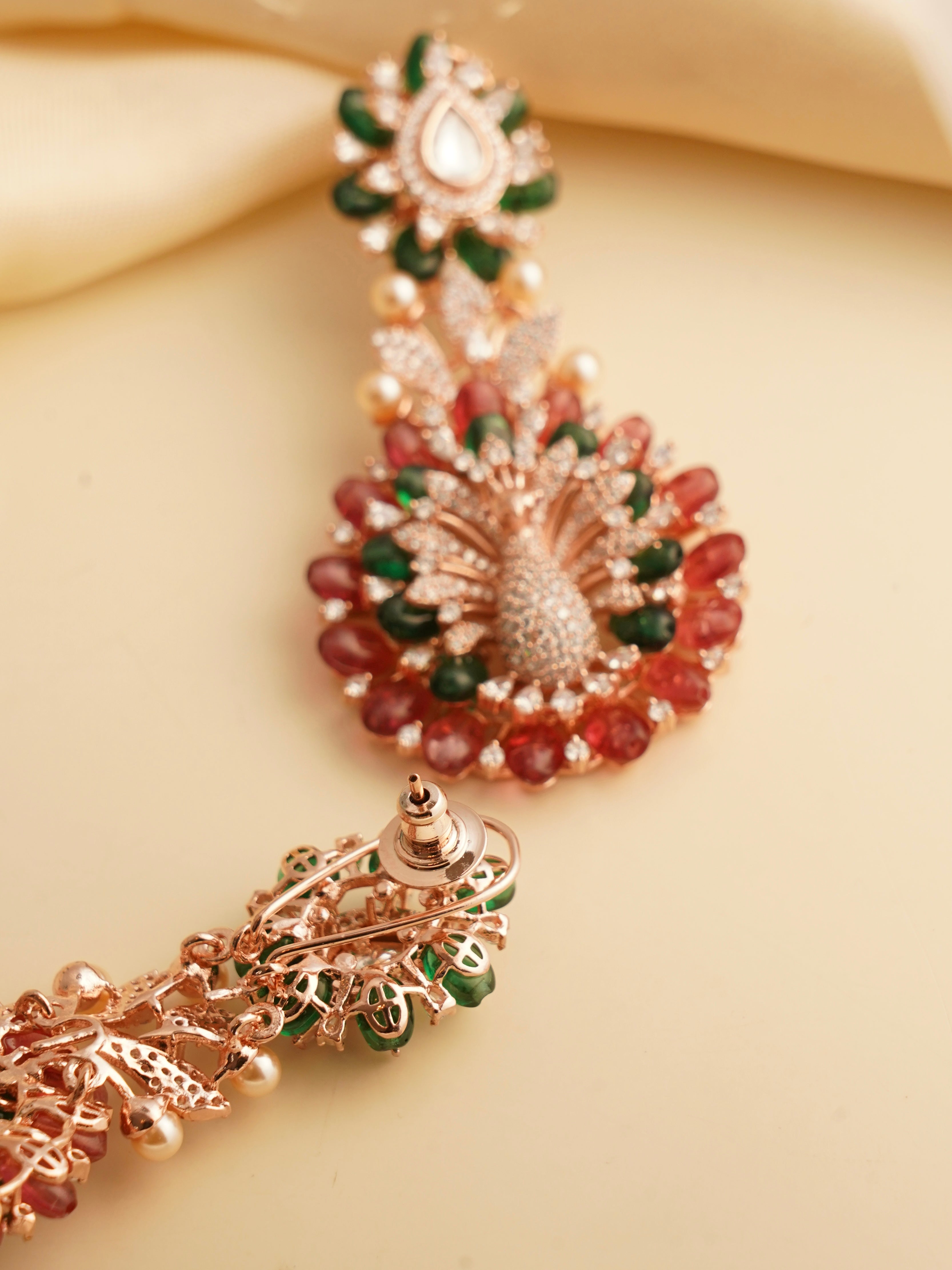 angled view of colorful beaded earrings with gold finish in peacock styling