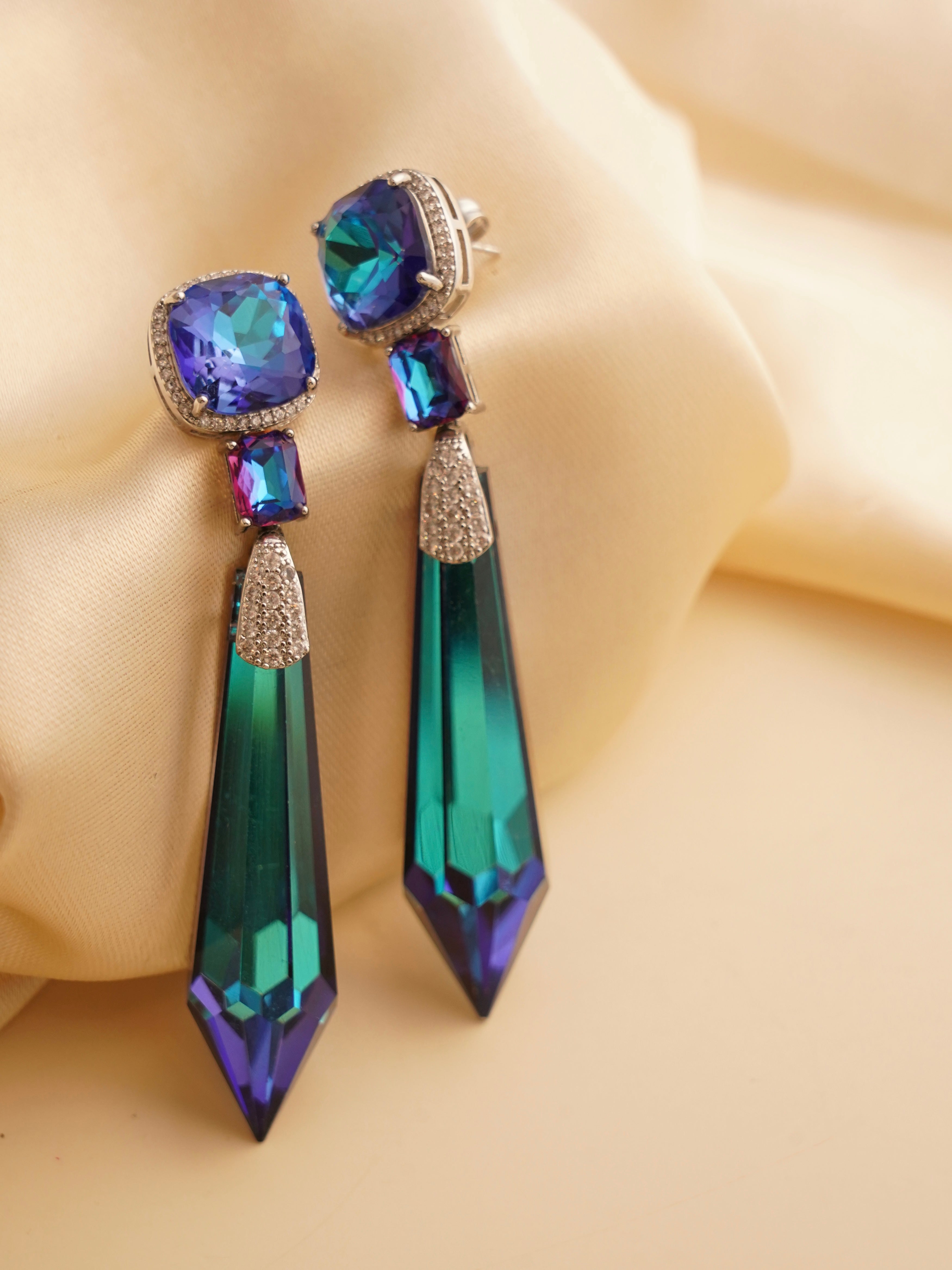 Prism earrings with angular drop silhouette, catching light in cosmic blue and amber shades