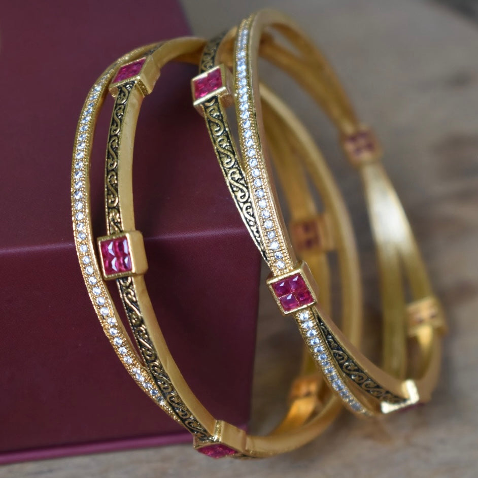Gold-tone bangles with black enamel filigree and square ruby-colored stones