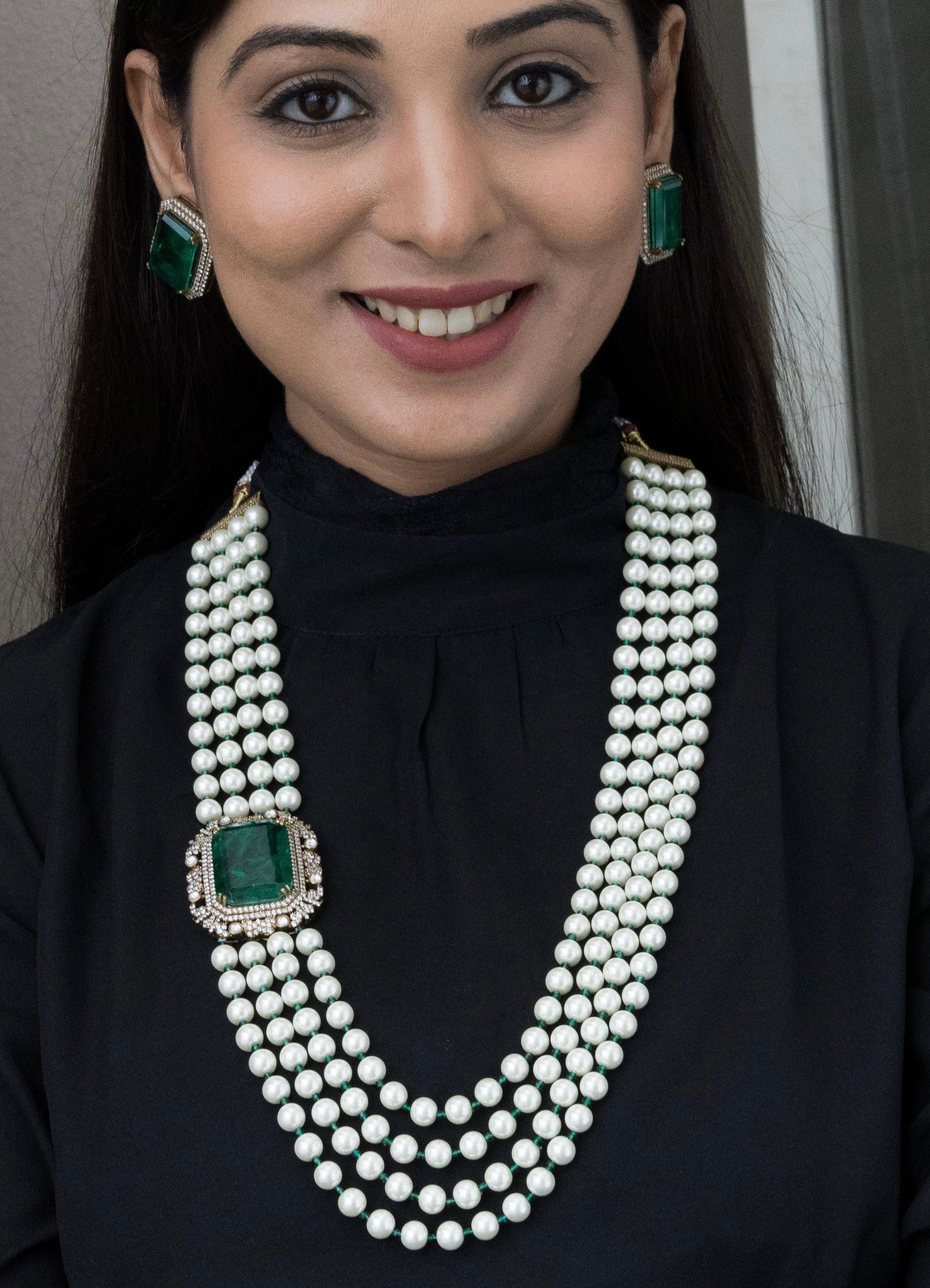 Close-up of pearl necklace with emerald-green stone accents and intricate beaded detailing