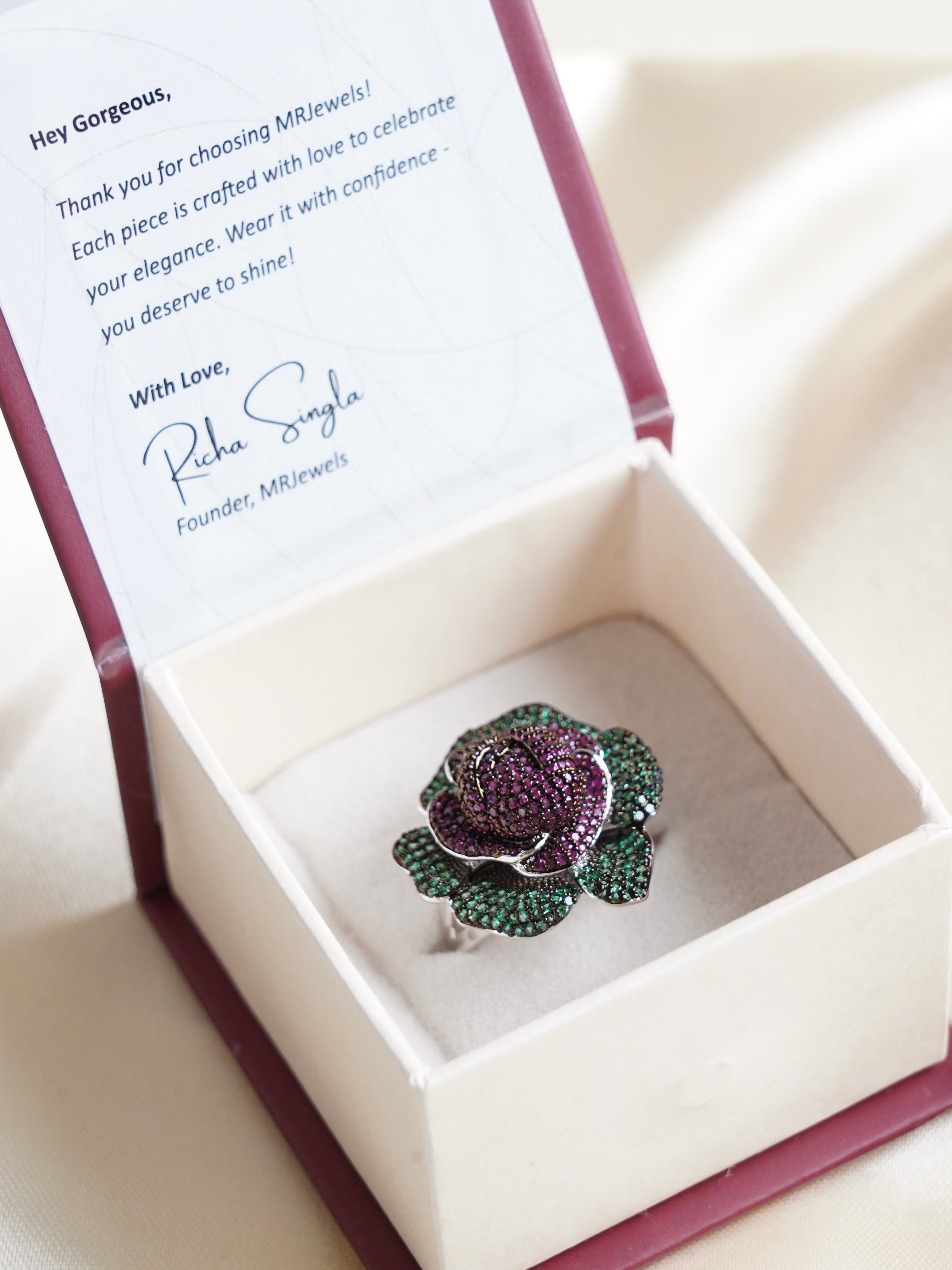 Blooming rose cocktail ring with purple gemstone petals and green leaf detailing in floral silhouette