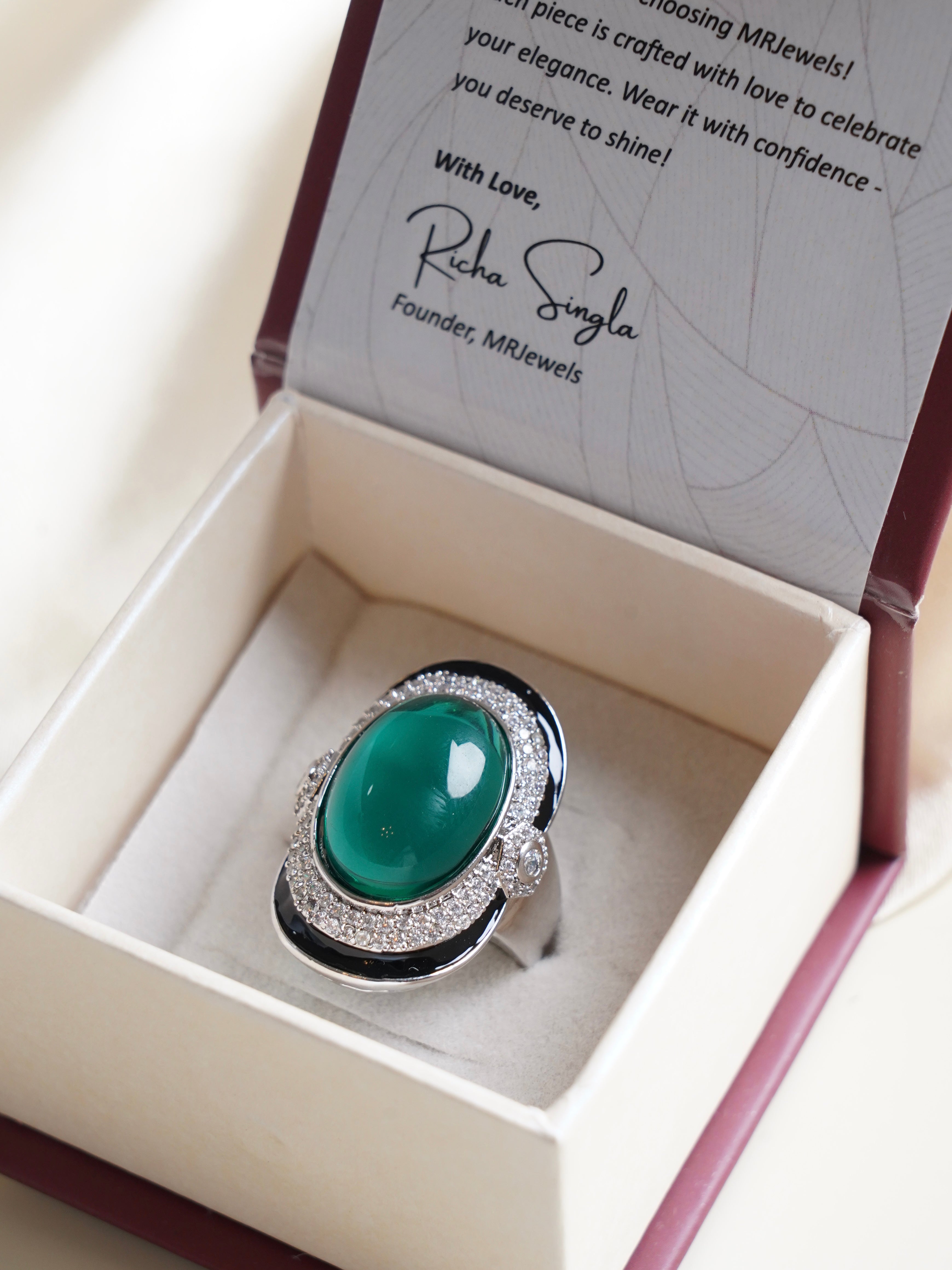 Emerald Mirage cocktail ring with oval green cabochon, zircon halo and black enamel border in jewellery box