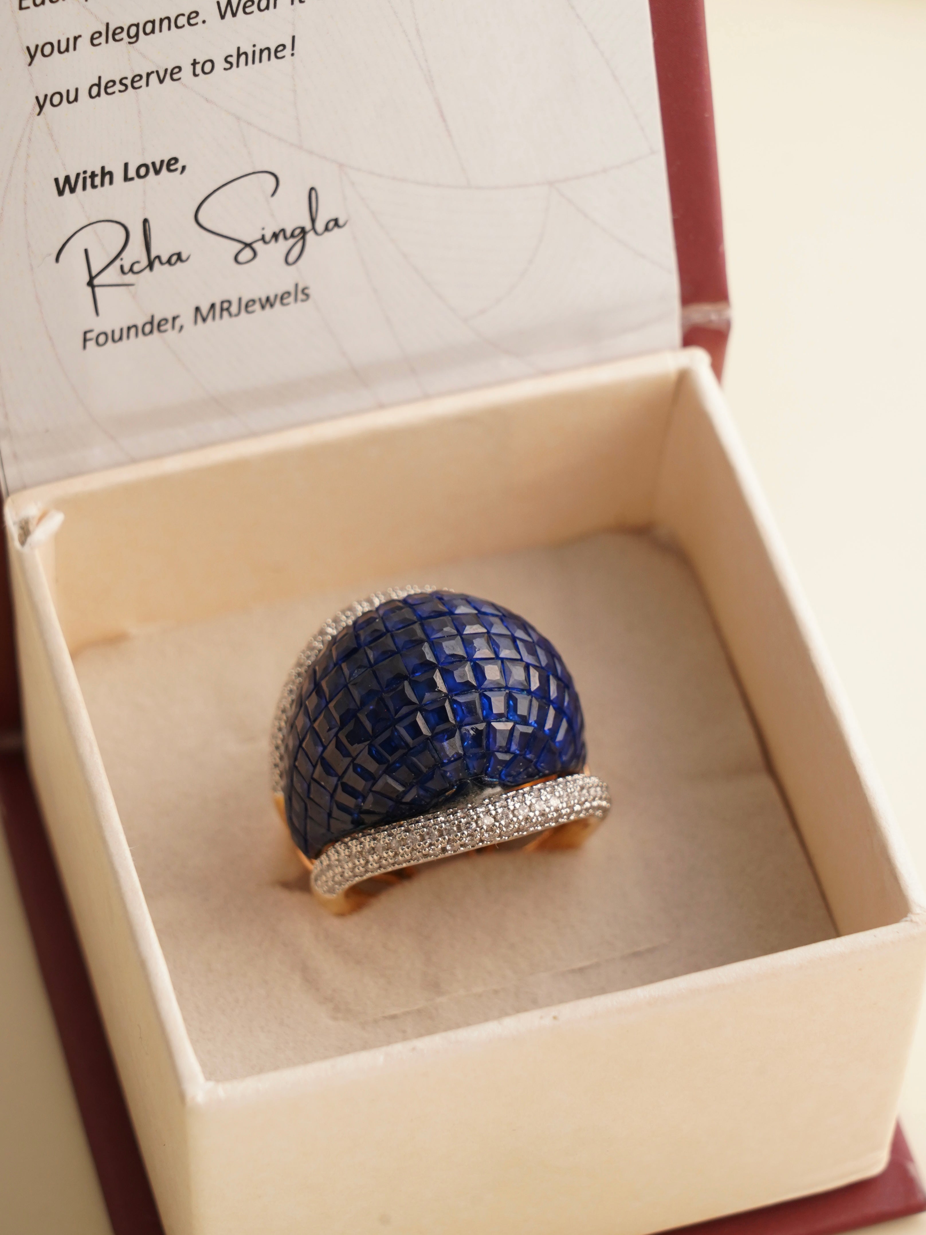 Close-up of gold-plated ring showcasing dark blue mosaic stone and diamond sparkle