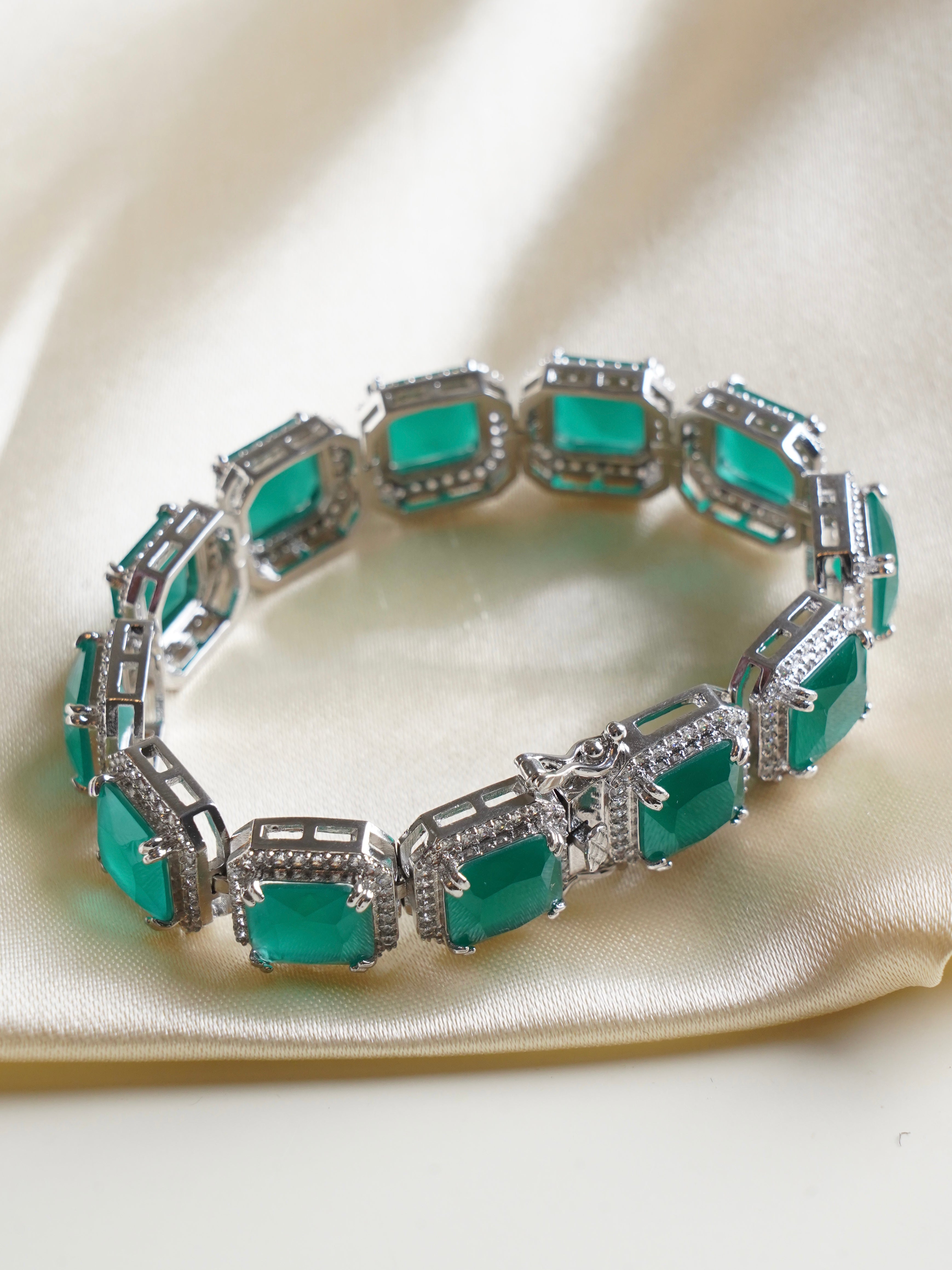 Close-up of emerald green bracelet showing sparkle of baguette studs in rhodium-plated frame