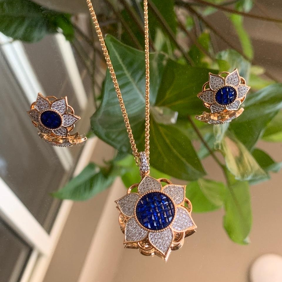 Angled view of floral pendant set with deep blue sapphire and CZ diamonds on gold plating