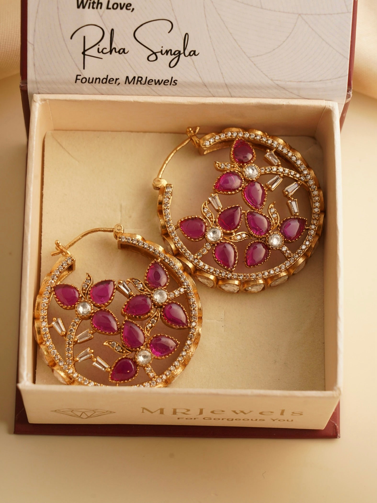 Side angle of pink gemstone hoops with intricate petal design and sparkling stone highlights