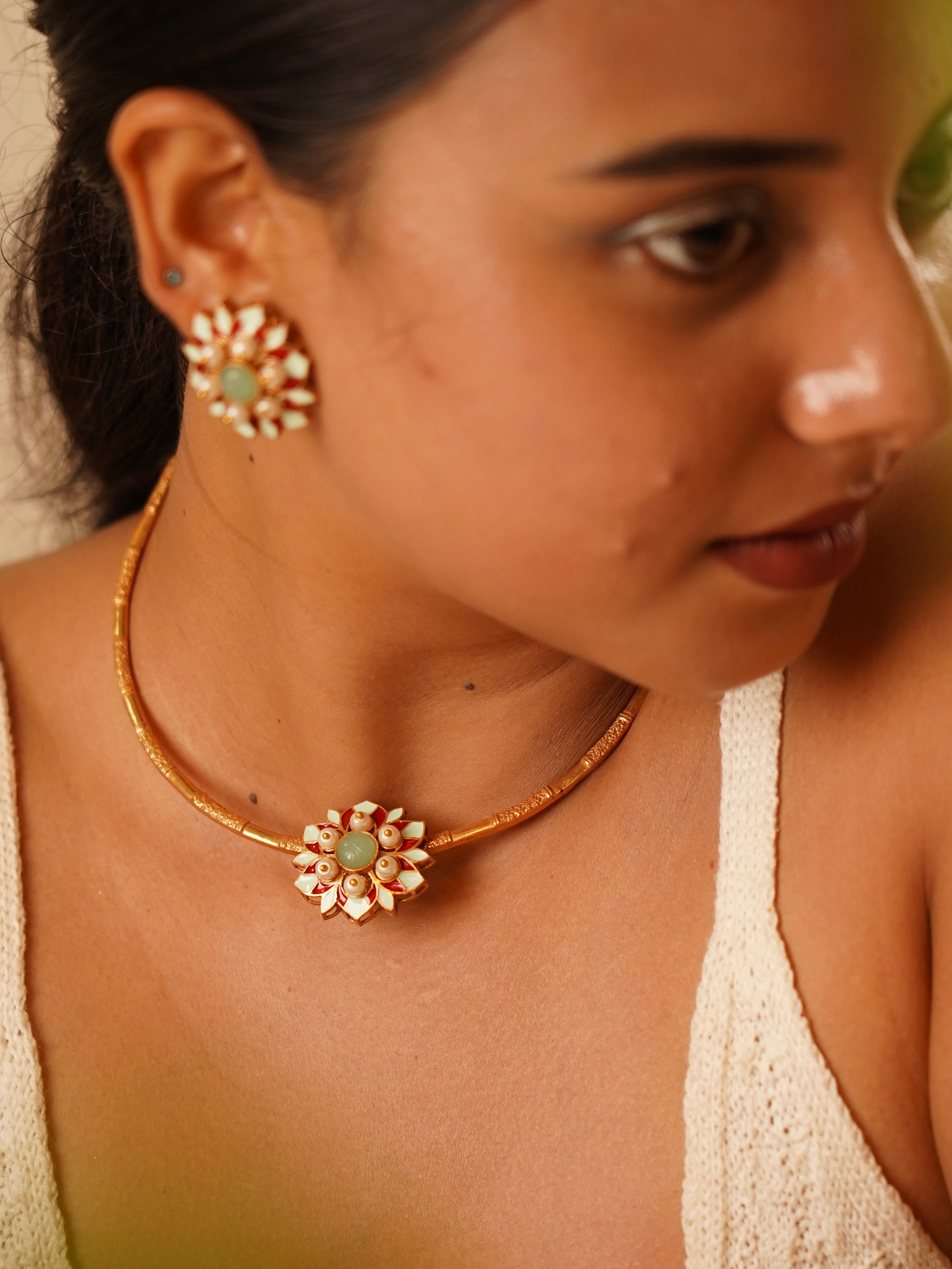 Model wearing Myra Muse hasli necklace with enamel floral motif in red and mint tones and matching stud