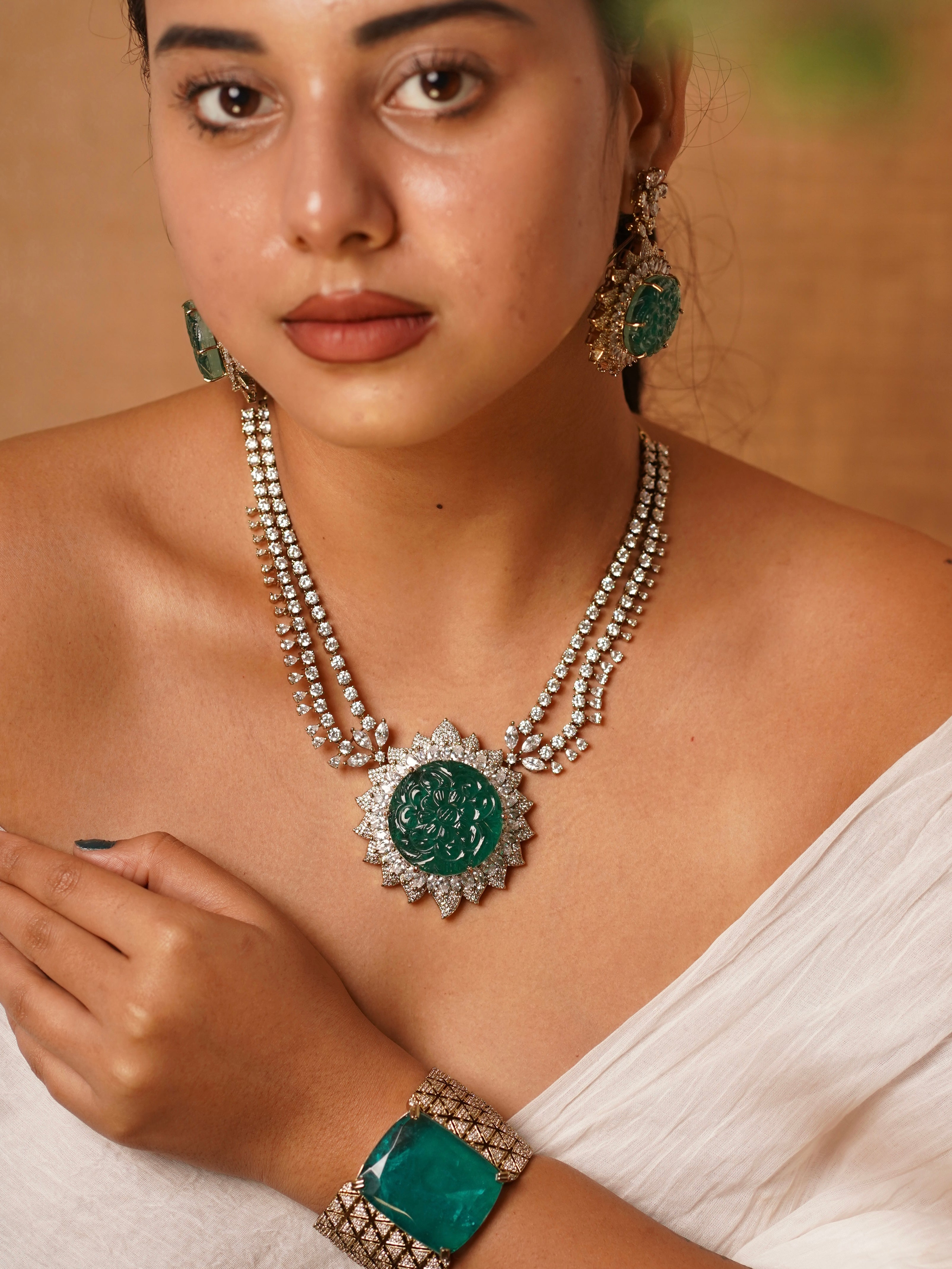 Side view of emerald medallion necklace set with floral CZ detailing and triple-strand gold-toned chains