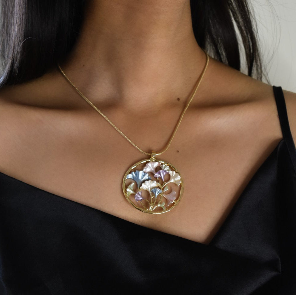 Angled view of enamel floral gold pendant with intricate detailing and polished finish