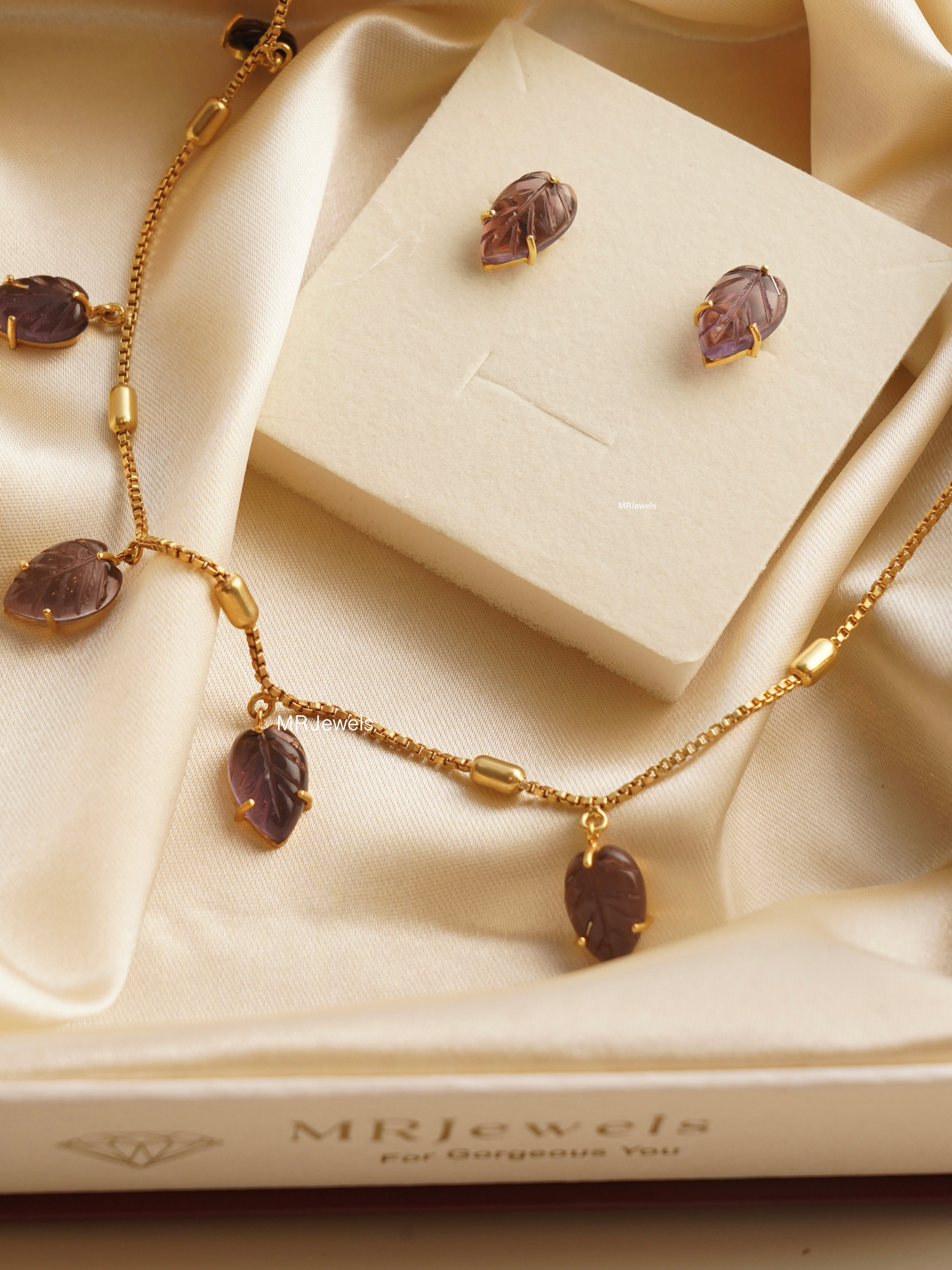 Close-up of gold necklace with garnet leaf charms and minimal chain design