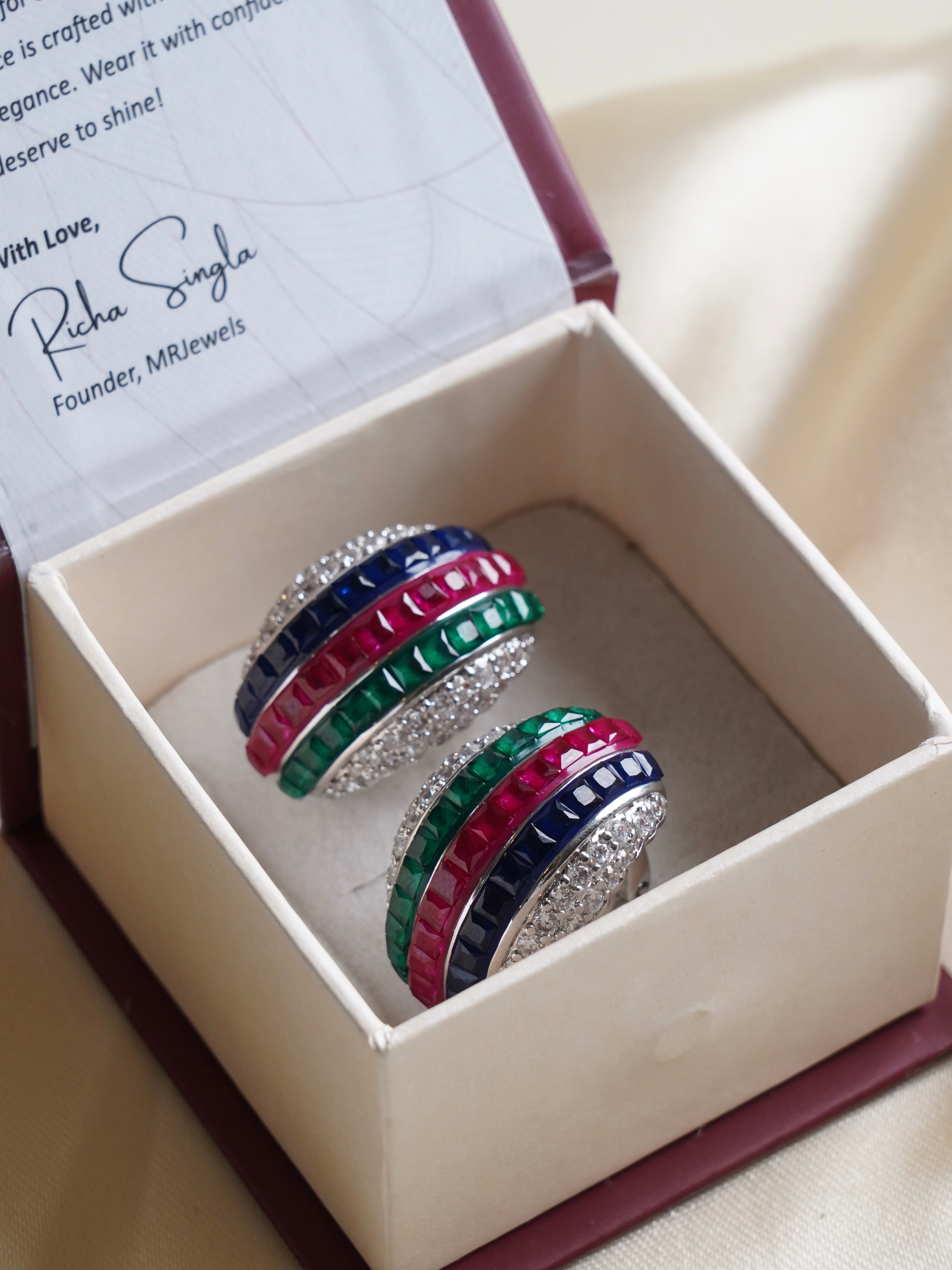 Front view of stud earrings featuring rich ruby center and vibrant emerald-sapphire accents