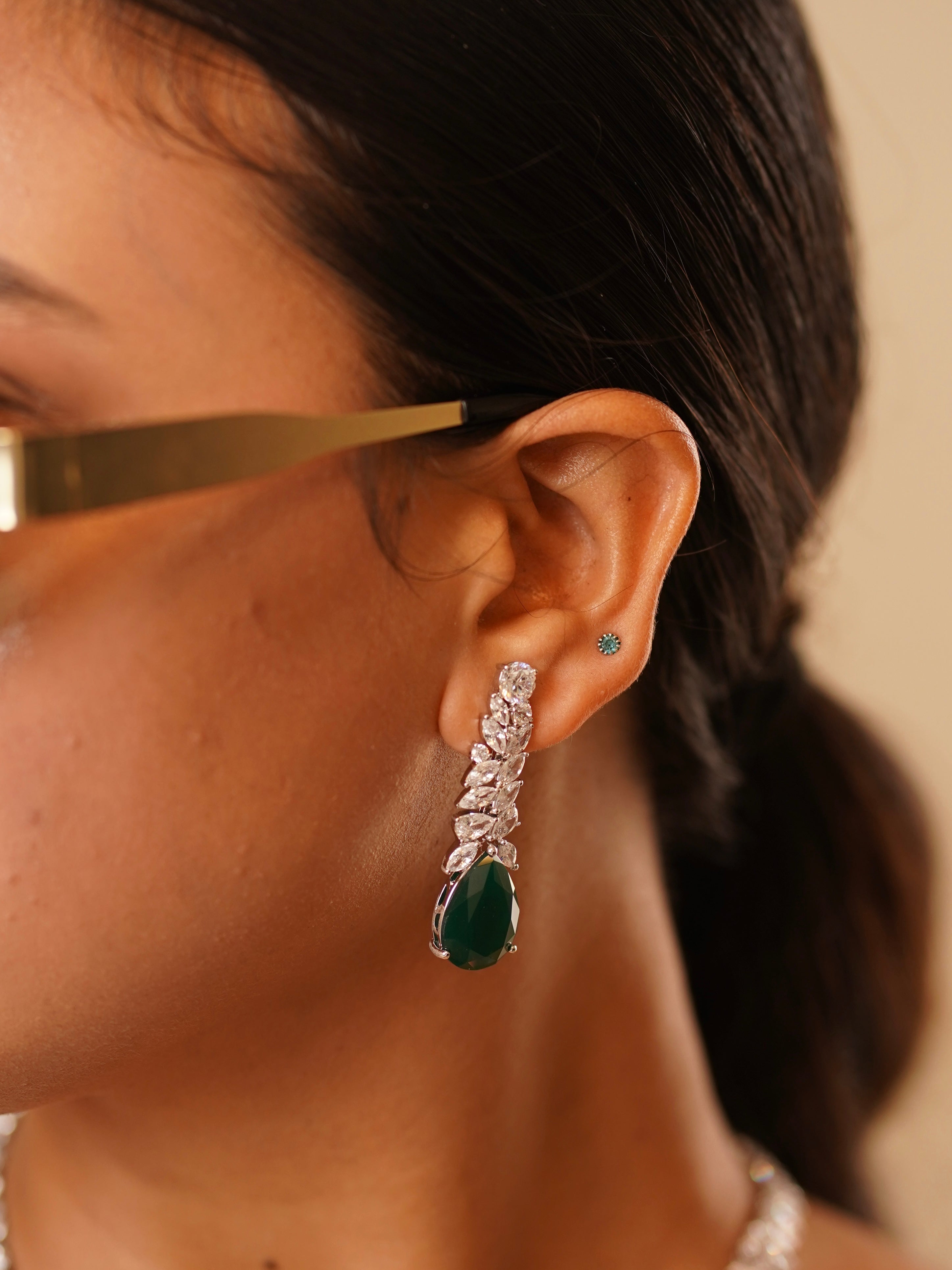 Side angle of royal emerald drop necklace with matching earrings featuring teardrop green stones