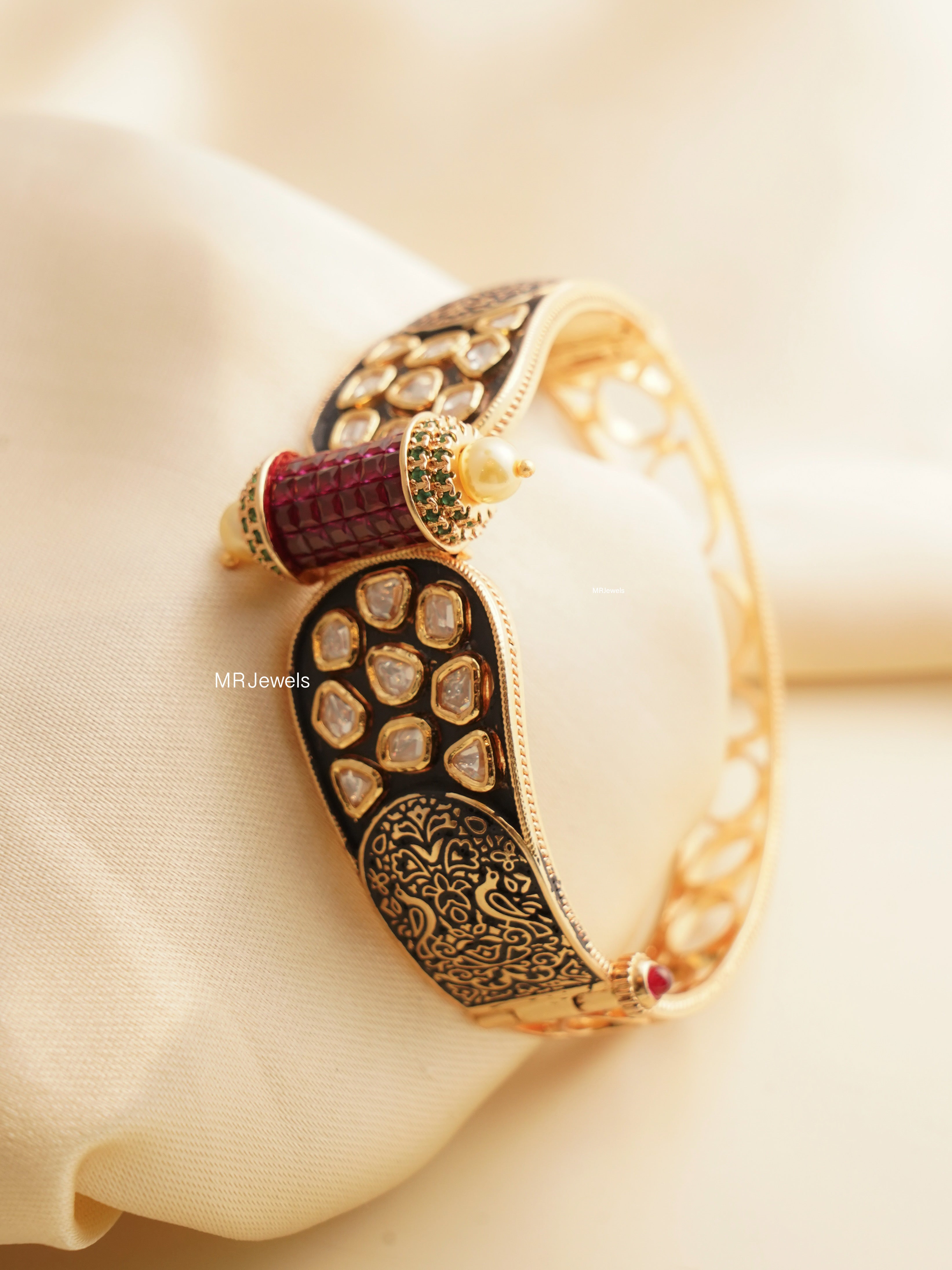 Angled view of gold bracelet with ruby enamel, Kundan stones, and vintage design
