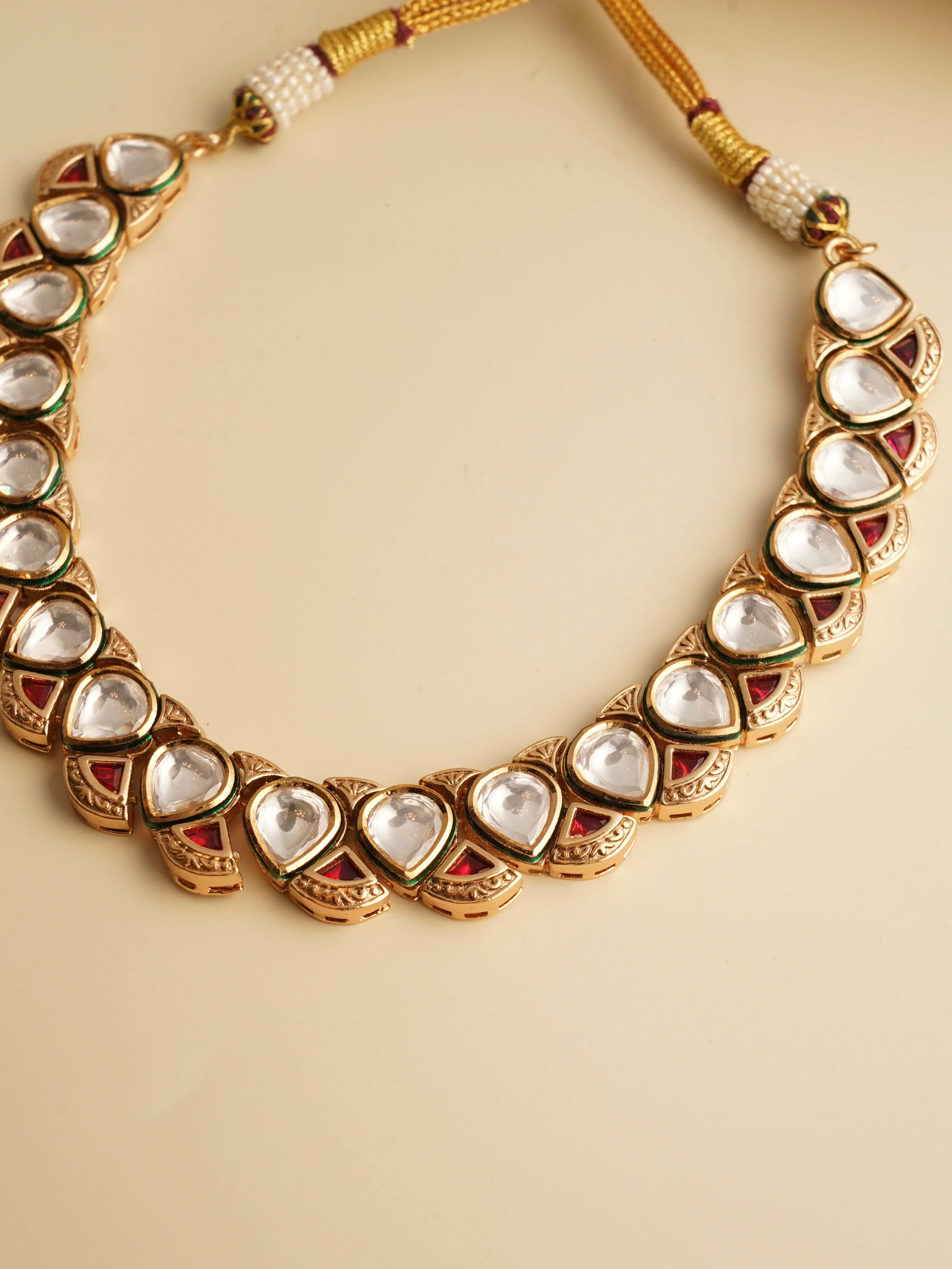 Close-up of kundan earrings with green and red enamel and teardrop motif