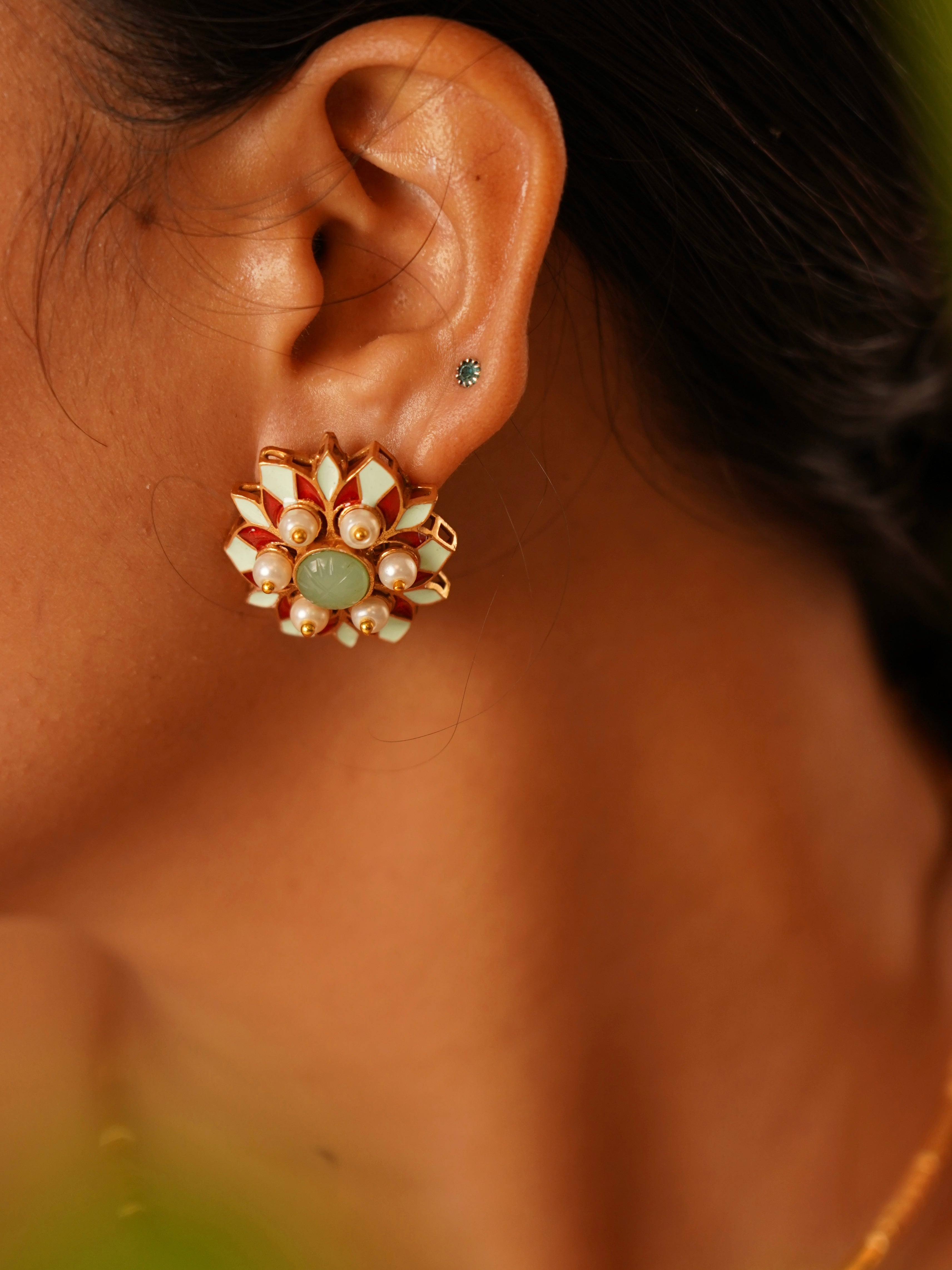 Close-up of Myra Muse floral stud with red and cream enamel petals, central stone and pearl clusters