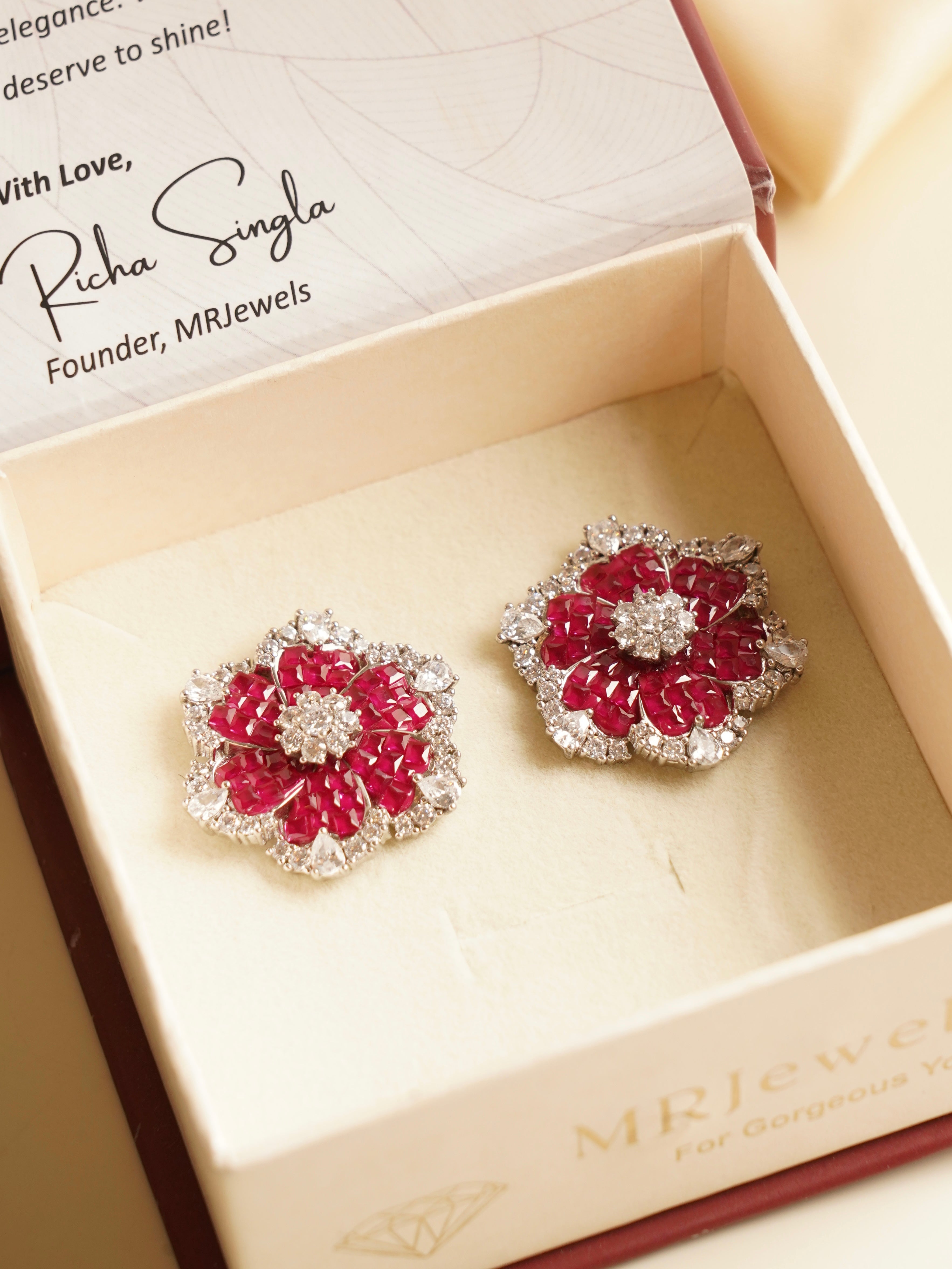 Angled close-up of emerald earrings with diamond detailing and floral motif