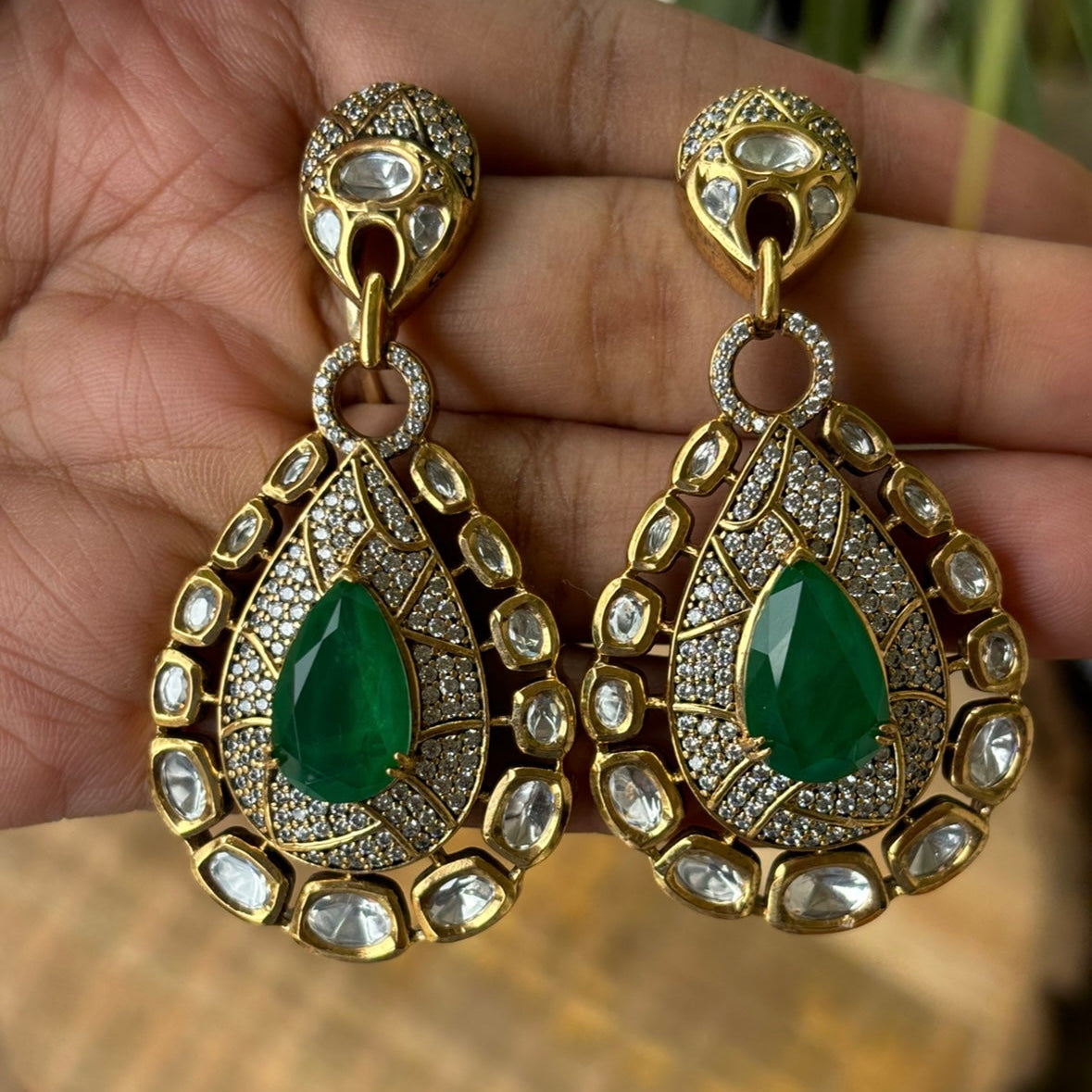 Angled image of royal-style statement earrings with gold finish and gemstone center