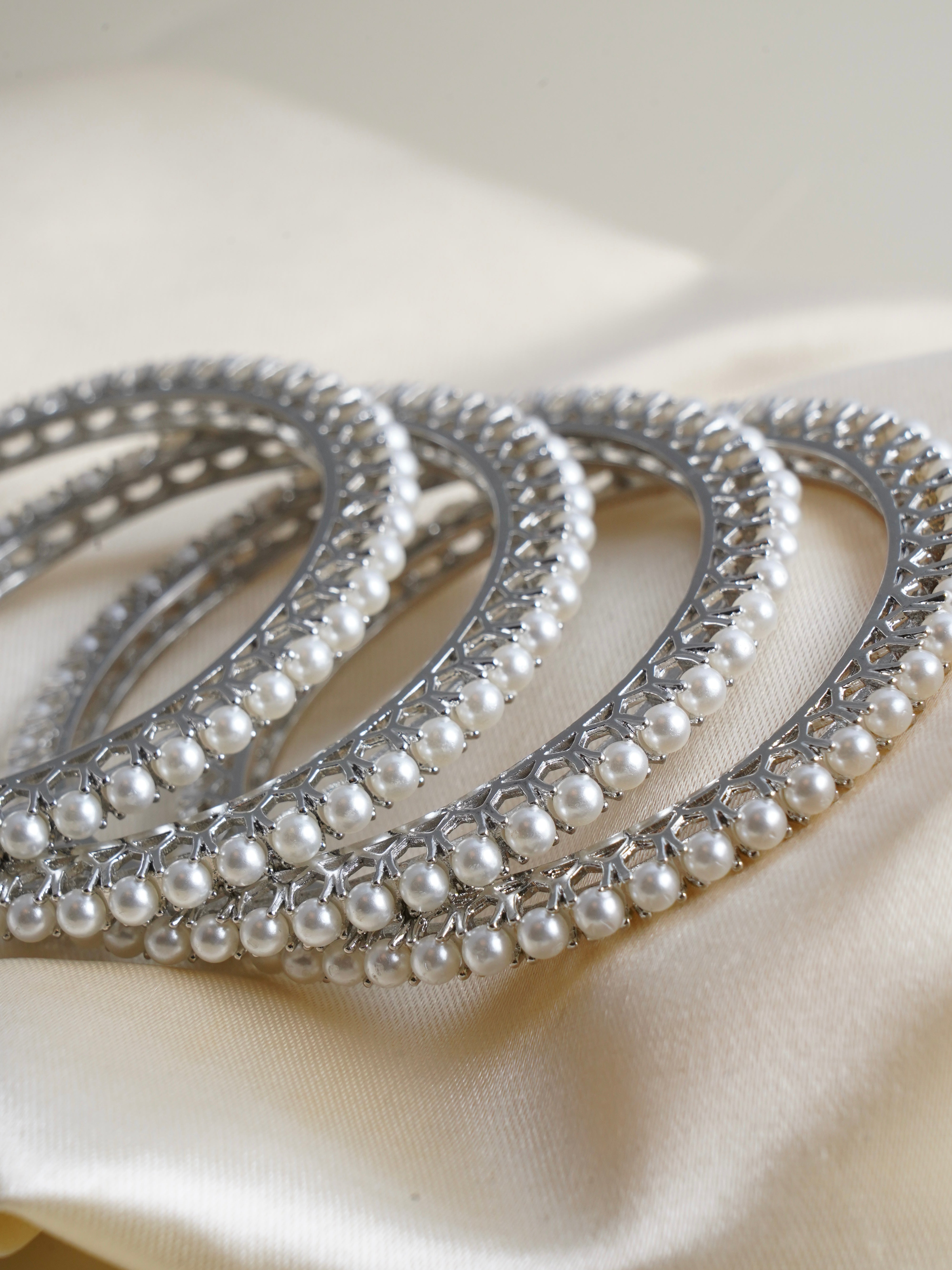Stacked bangles in silver and gold finish featuring symmetrical pearl accents and polished texture