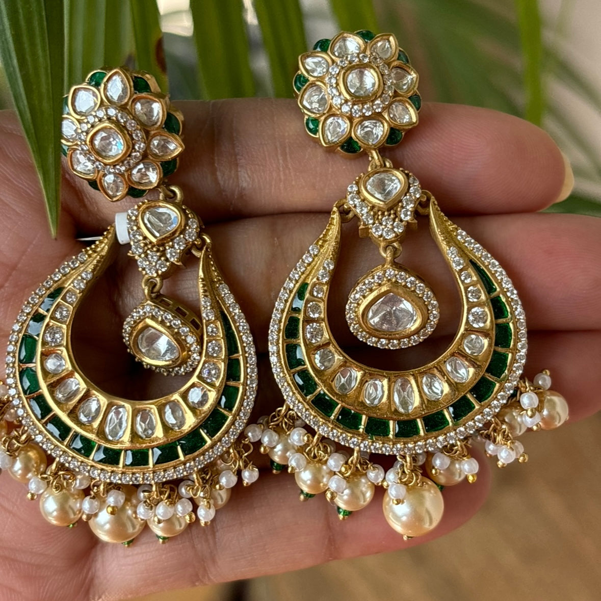 Close-up of kundan crescent earrings with green enamel and teardrop finish