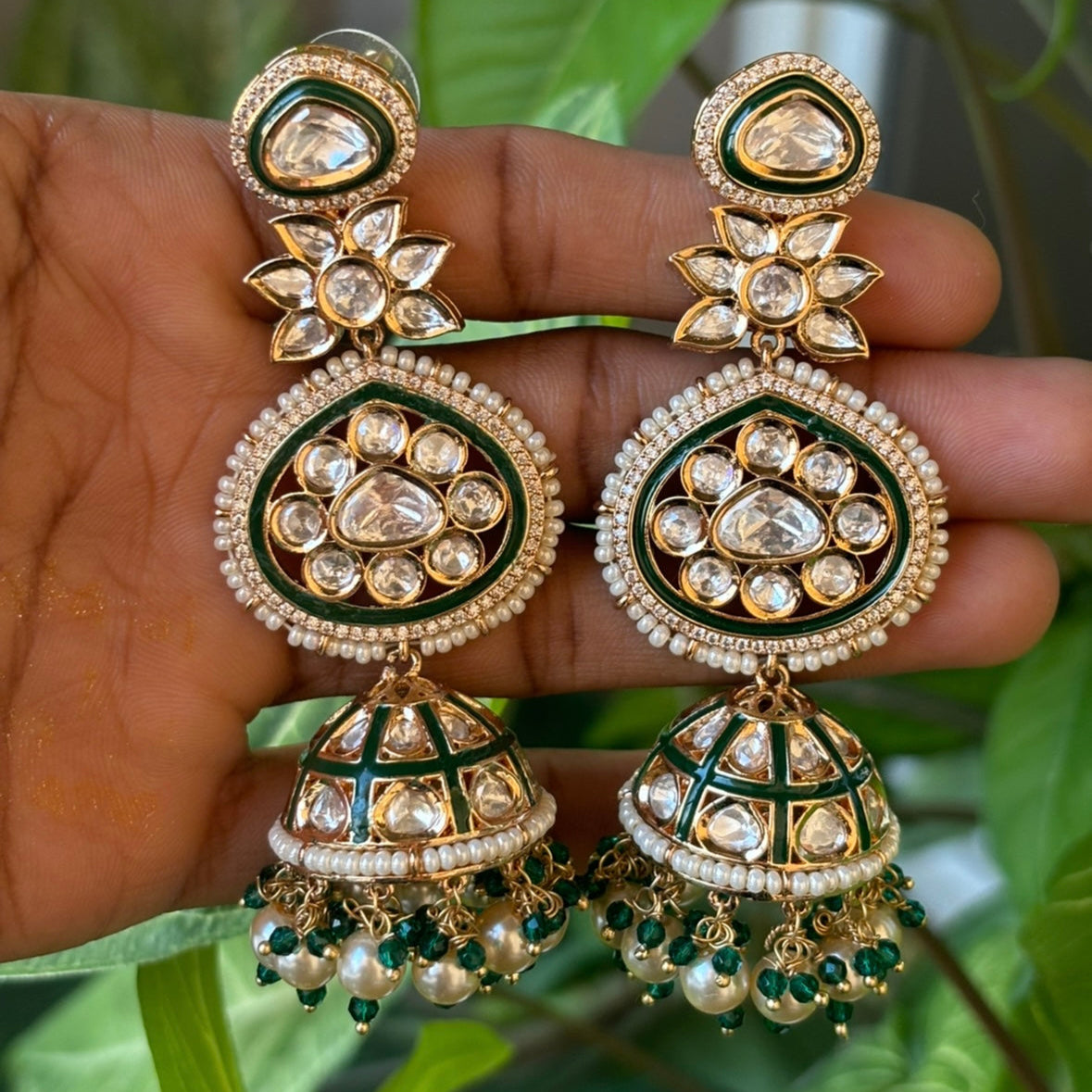 Angled view of emerald jhumkas with detailed enamel and sparkling stones