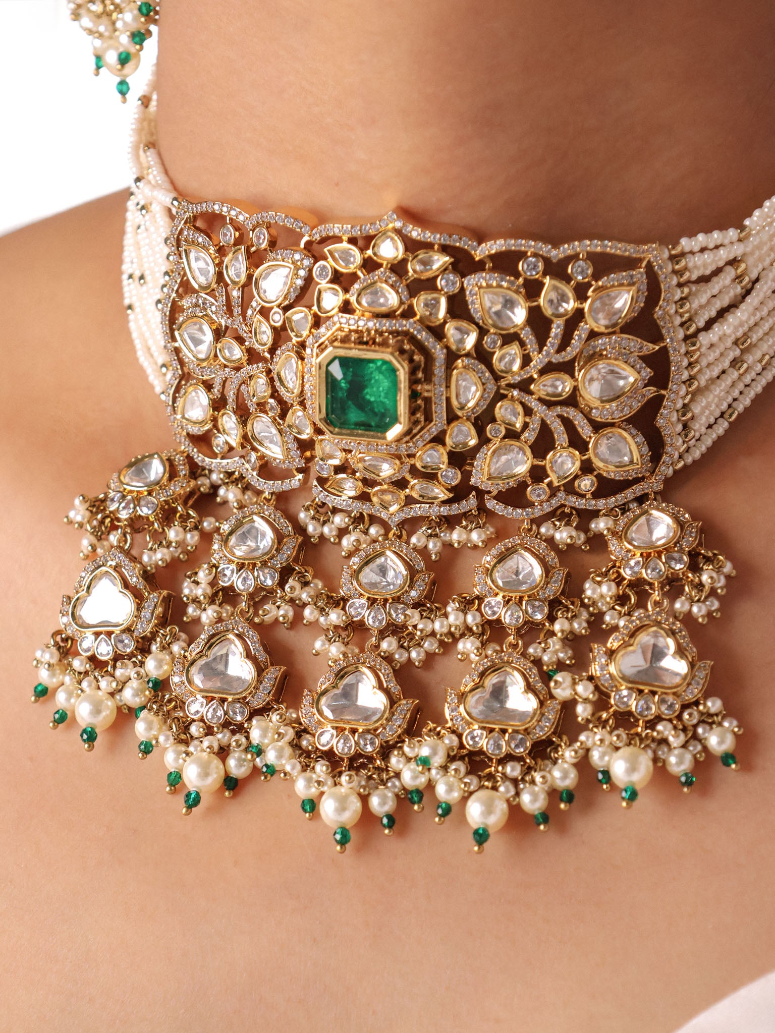 Close-up of an ornate necklace with emeralds and pearls on a person's neck.