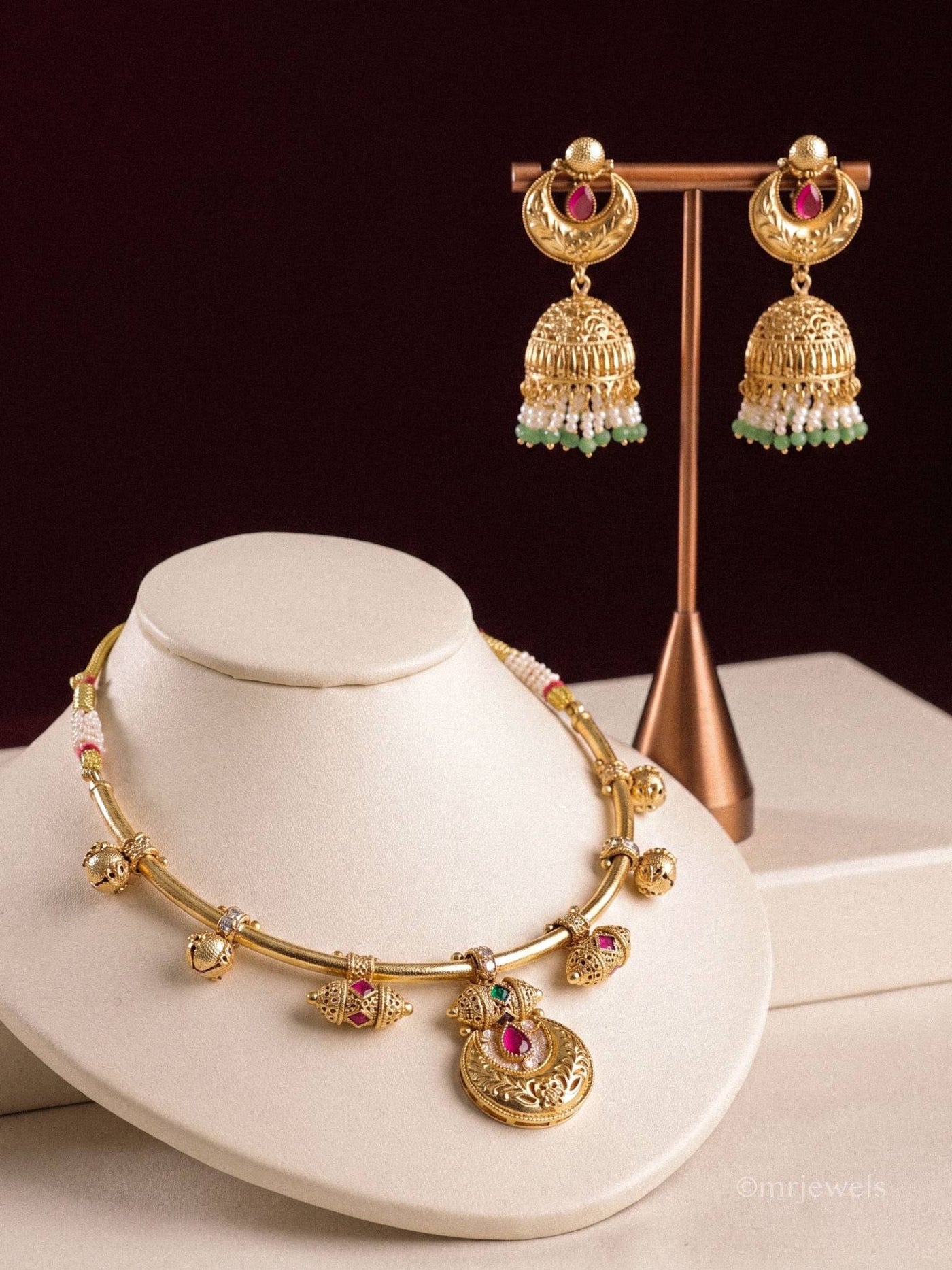 Gold-toned necklace and matching earrings on cream and burgundy display stands